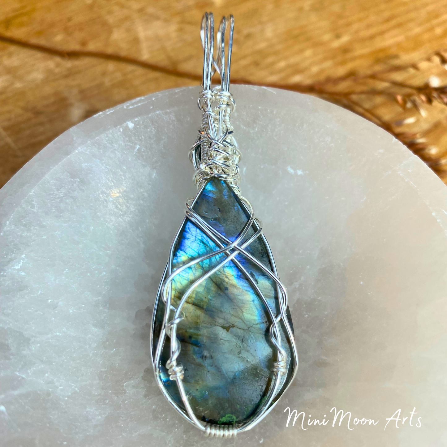 Transform and evolve Labradorite and malachite wire wrapped silver wire pendant back view in a selenite bown and wooden table background