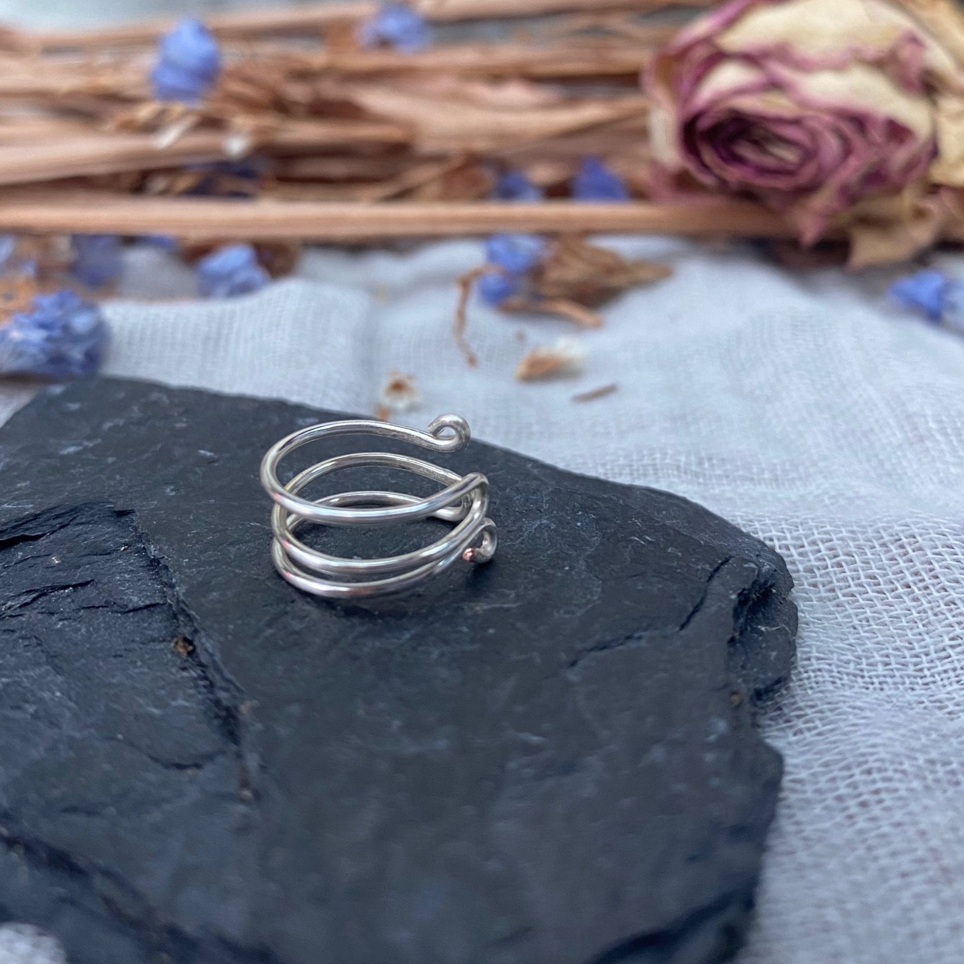 silver adjustable ear cuff sat on a piece of slate with dried rose and purple flowers in back ground